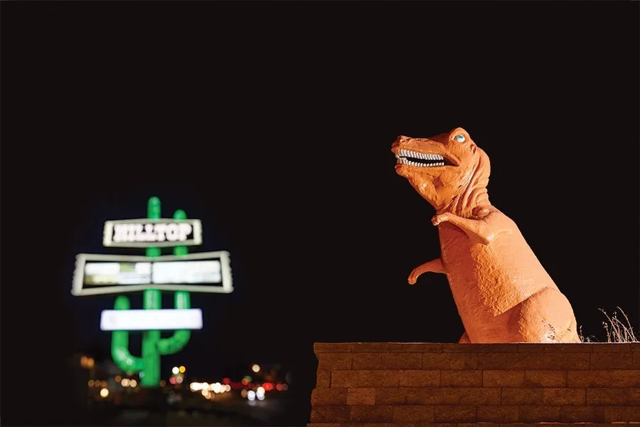 The Hilltop cactus sign and an orange dinosaur statue at night
